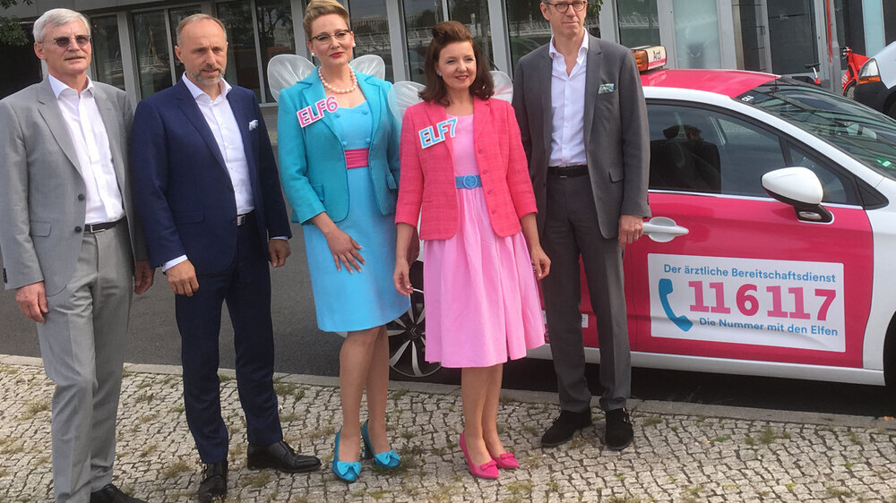 Der KBV-Vorstand Dr. Thomas Kriedel, Dr. Stephan Hofmeister und Dr. Andreas Gassen posiert mit den "Elfen" vor einem Auto des Berliner Bereitschaftsdienstes, das bereits das neue Logo der 116117 trägt.