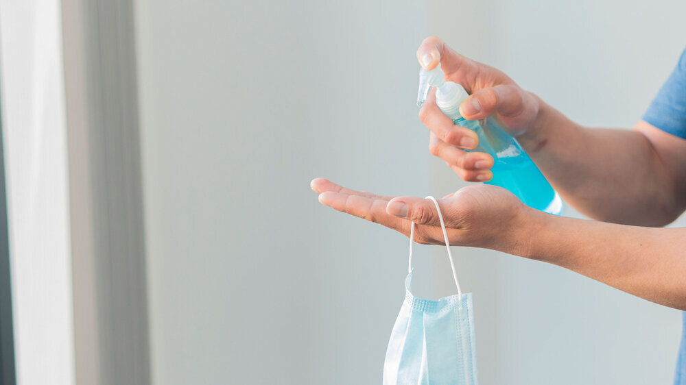The hand of a young man sprayed a disinfectant onto his hand and a mouth guard hung on his hand.