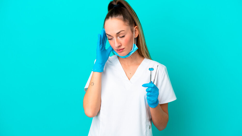 Zahnärztin auf blauem Hintergrund mit Kopfschmerzen hält Instrumente