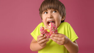 Lustiger kleiner Junge beißt in Donut vor farbigem Hintergrund