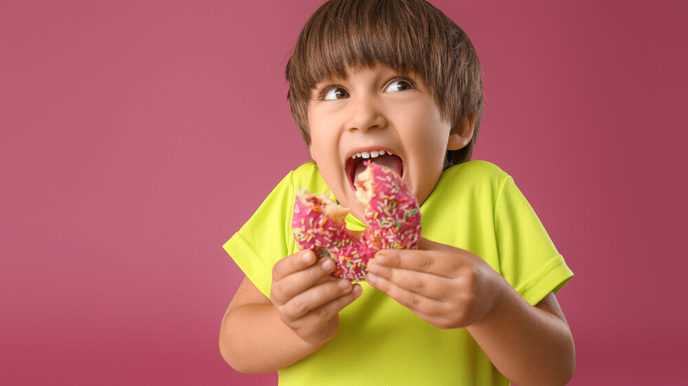 Lustiger kleiner Junge beißt in Donut vor farbigem Hintergrund