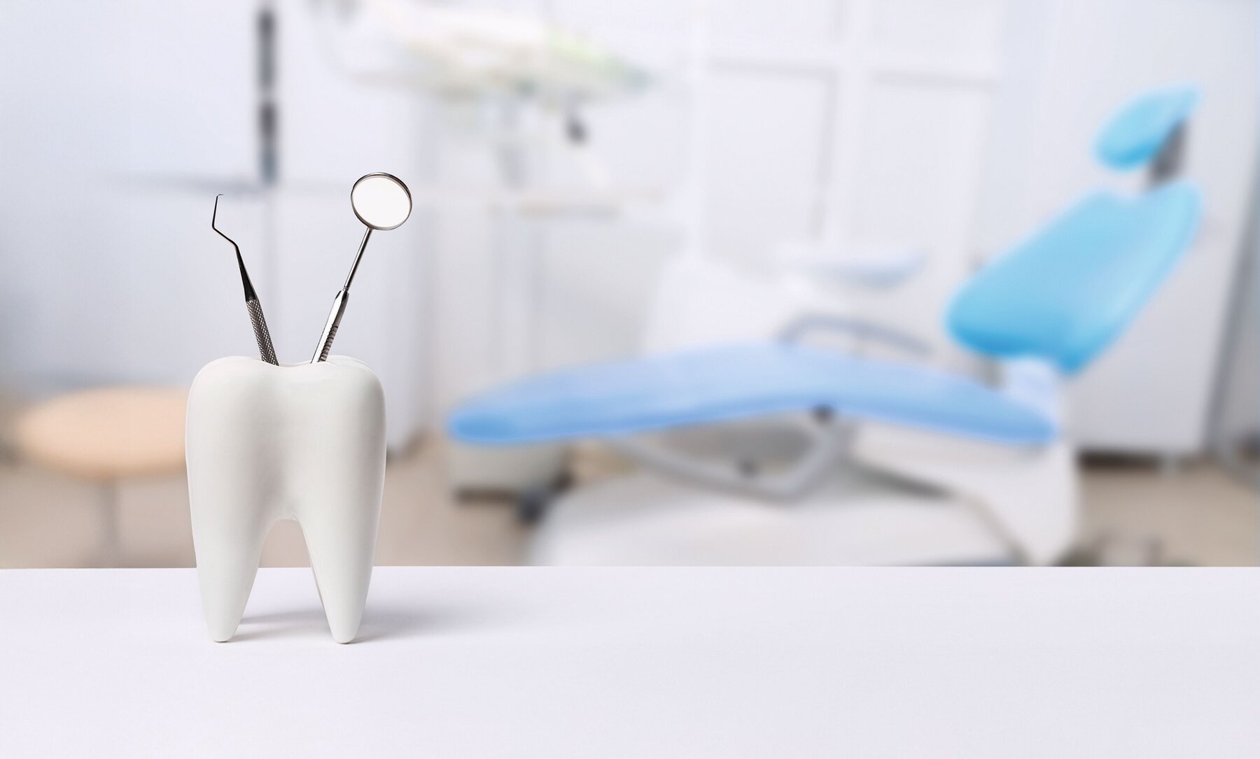 Oral dental hygiene. Healthy white tooth and dentist mirror with explorer probe instrument against blurred dentist Office background with dental chair.