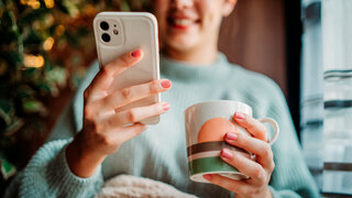 Young caucasian woman use phone send sms text messages and drink coffee by the window