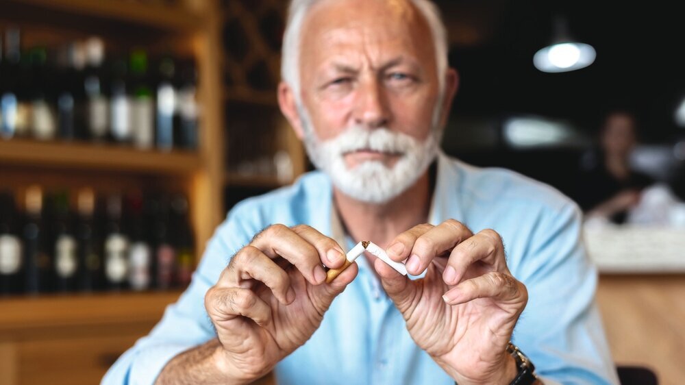 Senior man breaking cigarette as it is injurious to health Älterer Mann zerbricht Zigarette