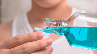 Hand, die eine Flasche Mundwasser in die Kappe gießt.