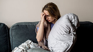 young woman with long covid syndrome - painful condition, headache, sitting on the couch at home