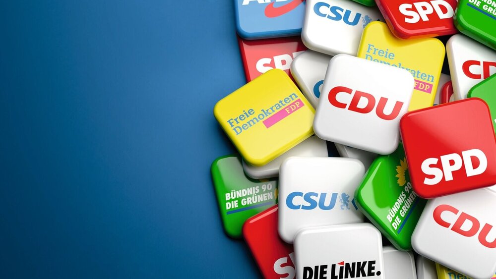 Logos of the biggest German political parties (CDU CSU, SPD, Die Grünen, FDP, Die Linke, AfD) running for the Bundestag election on a heap on a table. Copy space.