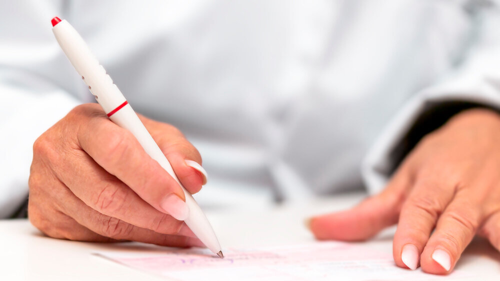 Ärztin beim Ausfüllen von Kassenrezept, rosa Rezeptformular für ein Medikament Ärztin beim Ausfüllen von Kassenrezept, rosa Rezeptformular für ein Medikament