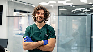 Proud young dental surgeon wearing green medical uniform posing for portrait photo in his clinic.