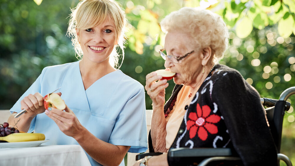 Pflegerin mit Seniorin beim Obstschälen