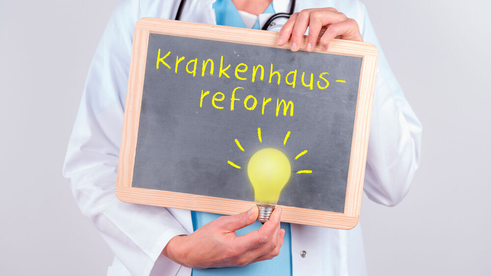 Ärztin mit einer Tafel auf der Krankenhausreform steht mit einer Glühbirne die leuchtet. Konzept Ideen in der Reformfindung Bei der geplanten Krankenhausreform soll es Öffnungsklauseln für die Länder geben.