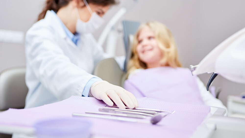 Zahnmedizinische Fachangestellte greift Instrumente neben junger Patientin.