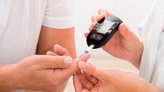 Nahaufnahme von Arzt, der einem älteren Patienten den Blutzuckerspiegel misst.