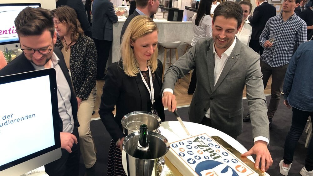 Der BdZA-Vorsitzende Ingmar Dobberstein und Kassenwart Juliane von Hoyningen-Huene schneiden auf der IDS am BZÄK-Stand die Geburtstagstorte an.