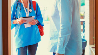 Female doctor with clipboard during home visit while entering house.