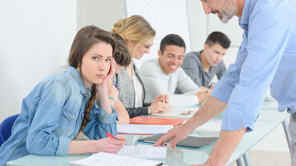 Mädchen sitzt im Unterricht und schaut frustriert in die Kamera