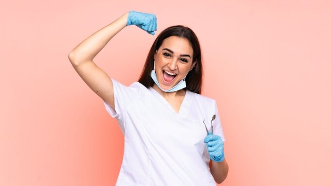 Woman dentist holding tools isolated on pink background celebrating a victory Woman dentist holding tools isolated on pink background celebrating a victory