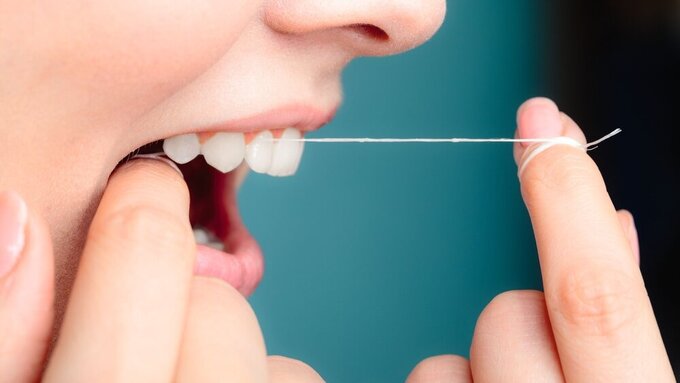 side view woman face smiling with dental floss. Wenn die Zahnseide butterweich flutscht, könnte es an Per- und polyfluorierten Alkylsubstanzen (PFAS) liegen, die mit zahlreichen gesundheitlichen Problemen in Verbindung gebracht werden..