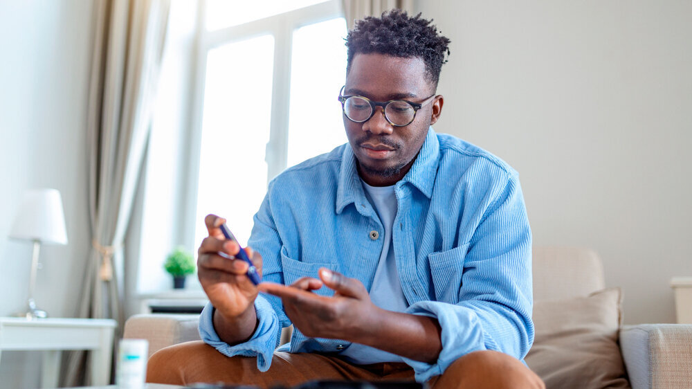 Ein afrikanischer Mann sitzt auf dem Sofa und nimmt sich aufgrund seiner Diabeteserkrankung Blut aus dem Finger.