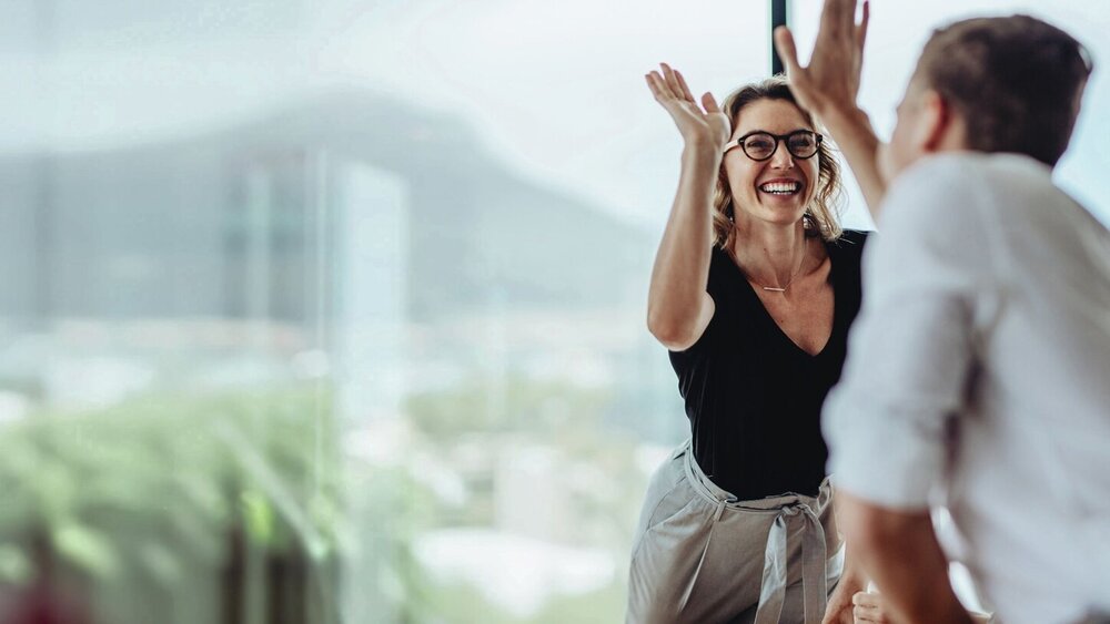 Geschäftsfrau gibt einem Kollegen in einer Besprechung ein High Five.