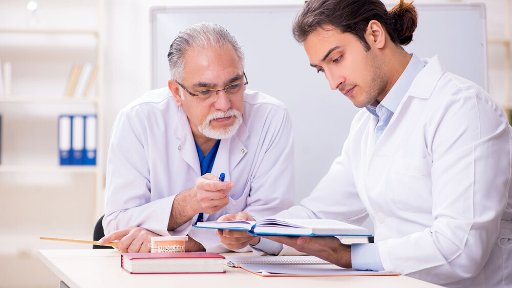 Experienced doctor dentist teaching young male assistant junger und alter Zahnarzt im Büro