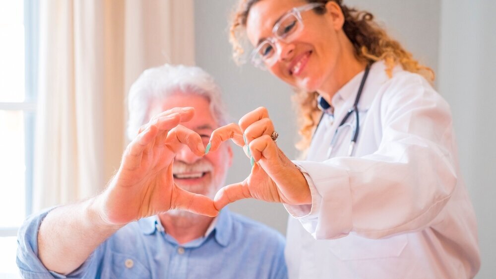 Close up of young female doctor and senior man showing heart sign with hand at home. Doctor helping senior patient and giving care. Elderly medical health care. In welchem Bundesland gibt es die höchste Dichte an zufriedenen Patienten, wenn es um die Gesundheit und die medizinische Versorgung geht?