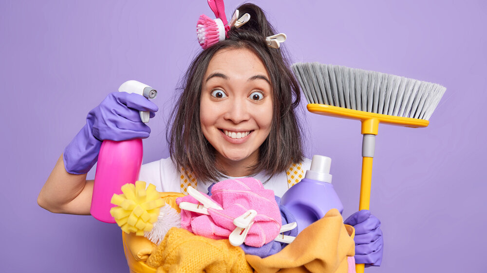 Cleanup and washing time concept. Cheerful surprised young Asian woman poses with dispenser and broom supplies regular cleaning of house washes laundry uses chemical detergents poses indoor. Putzen