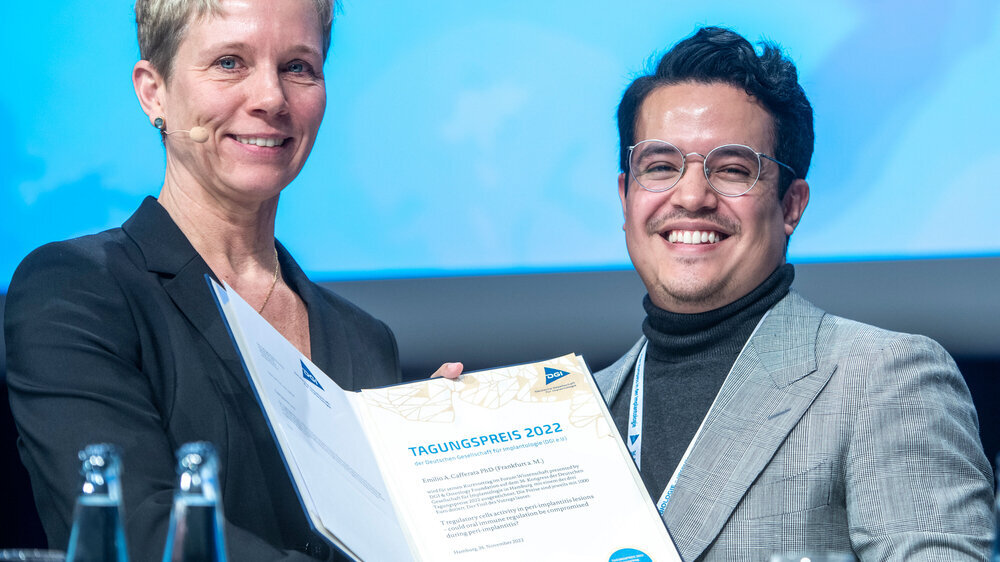 Veränderte Regulation der Immunantwort bei Periimplantitis\r\n Emilio Cafferata PhD von der Abteilung für Zahnärztliche Chirurgie und Implantologie der Goethe-Universität Frankfurt/Main hat untersucht, ob die Regulation des Immunsystems bei einer Periimplantits gestört ist. Dazu analysierte der Wissenschaftler im periimplantären Granulationsgewebe und im gesunden periimplantären Gewebe die Aktivität verschiedener Immunzellen. \r\n Dabei handelt es sich um die sogenannten Regulatorischen T-Zellen, welche die pro-inflammatorische Achse der Immunantwort regulieren können. Ihre immunmodulierende, entzündungshemmende und damit knochenschützende Wirkung steht in Wechselwirkung mit bestimmten T-Helferzellen (Th17 Zellen), die proinflammatorisch wirken und daher die Knochenresorption fördern. \r\n Resultat: Zum ersten Mal zeigen diese Untersuchung, dass Regulatorische T-Zellen im periimplantären Gewebe aktiv sind und bestimmte Immunbotenstoffe produzierten. In diesen Proben waren mehr Regulatorische T-Zellen als im gesunden Gewebe sowie eine erhöhte Aktivität nachweisbar, die mit Th17-Zellen assoziiert ist. Fazit: Die Aktivität Regulatorischer T-Zellen ist bei einer Periimplantitis erhöht und verändert. Gleichzeitig können jedoch auch andere Signale des Immunsystems die Balance zwischen den Regulatorischen T-Zellen und den Th17-Zellen stören und so die Entzündung und den Knochenabbau bei einer Periimplantitis fördern. DGI-Vorstandsmitglied Dr. Anette Strunz überreichte auf der Tagung am 26. November 2022 die Urkunde für einen ausgezeichneten Kurzvortrag an Cafferata. \r\n