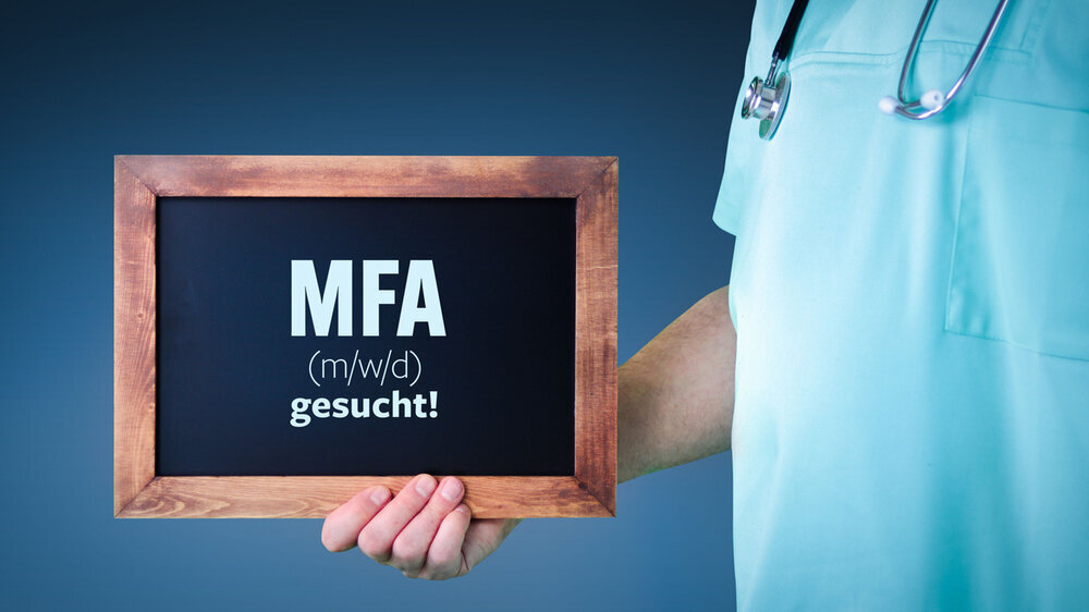 MFA (m/w/d) gesucht! (Medizinische Fachangestellte). Arzt zeigt Schild/Tafel mit Holz Rahmen. Hintergrund blau