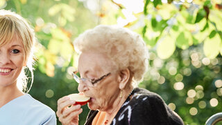 Pflegerin mit Seniorin beim Obstschälen