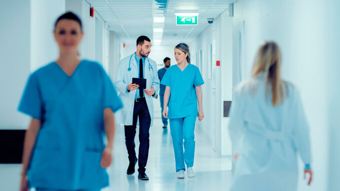 Surgeon and Female Doctor Walk Through Hospital Hallway, They Consult Digital Tablet Computer while Talking about Patient's Health. Modern Bright Hospital with Professional Staff. Ärzte im Krankenhaus