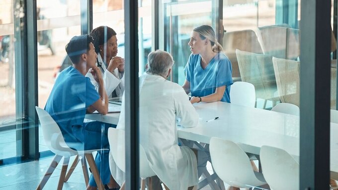 Doctors, healthcare team and meeting for a discussion, planning or training at table. Diversity men and women medical group talking about communication strategy, virus or surgery in a hospital Mitarbeitergespräch