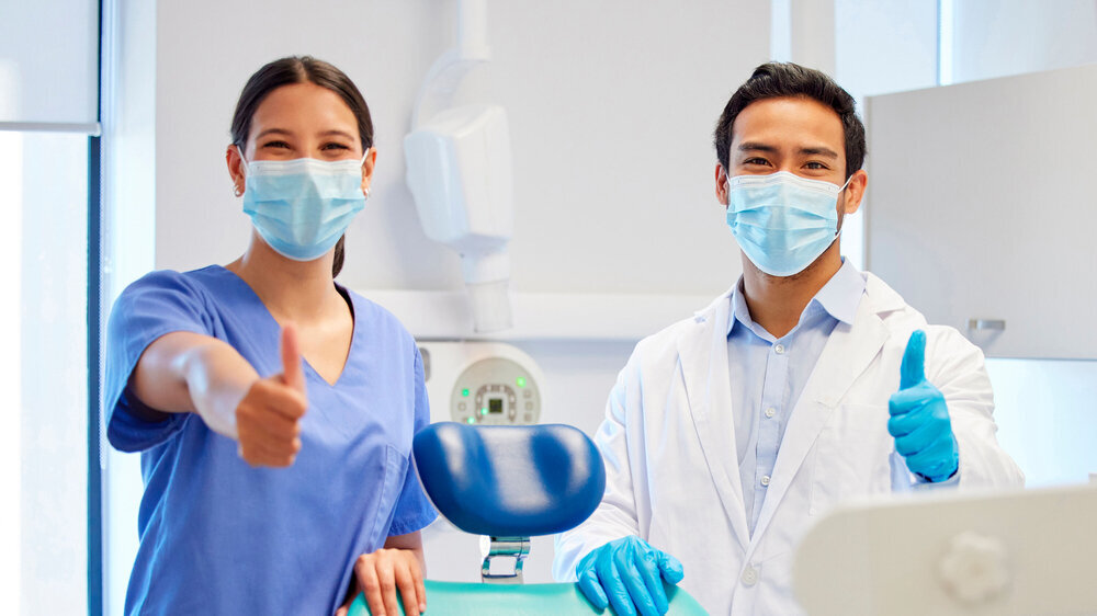 Dentist team, face mask and thumbs up portrait for.medical industry and teamwork. Assistant woman and asian man or healthcare staff together for dental care, oral health and wellness at practice.