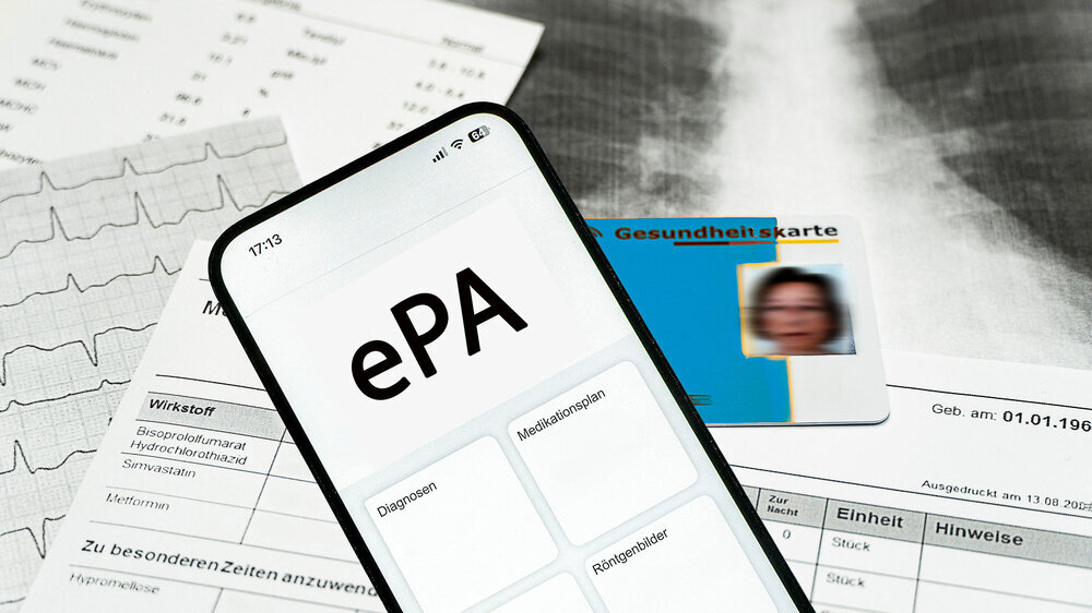 Ein Smartphone auf dem gerade eine elektronische Patientenakte angezeigt wird und eine elektronische Gesundheitskarte liegen Ein Smartphone auf dem gerade eine elektronische Patientenakte angezeigt wird und eine elektronische Gesundheitskarte liegen