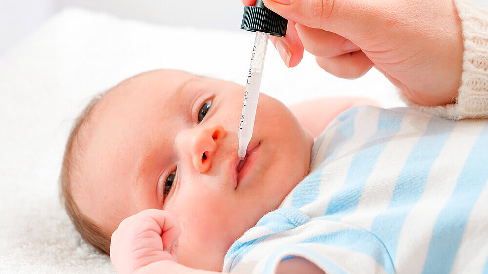 Closeup of mother giving vitamin D and K to her newborn baby son from eyedropper. Concept of babies and newborn vaccination and healthcare. Caring parents with little children. Closeup of mother giving vitamin D and K to her newborn baby son from eyedropper. Concept of babies and newborn vaccination and healthcare. Caring parents with little children