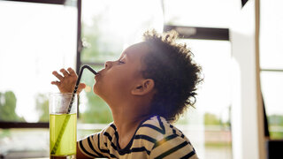 Kleiner Junge trinkt mit Strohhalm aus einem Glas gelber Limo.