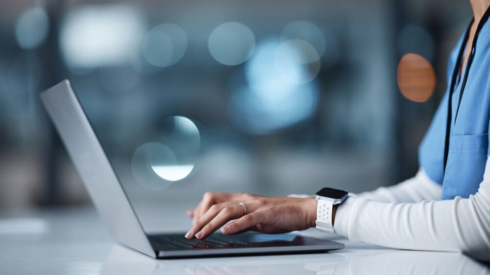 Nahansicht der Hände einer Ärztin, die blaue Arbeitskleidung trägt und an einem Laptop arbeitet. Nahansicht der Hände einer Ärztin, die blaue Arbeitskleidung trägt und an einem Laptop arbeitet.