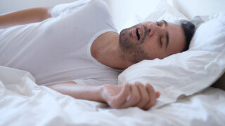 Mann schnarcht aufgrund von Schlafapnoe im Bett liegend.