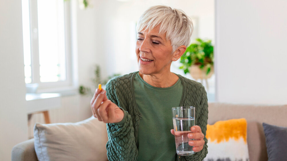 Ältere Frau hält Nahrungsergänzungskaspel in der Hand.