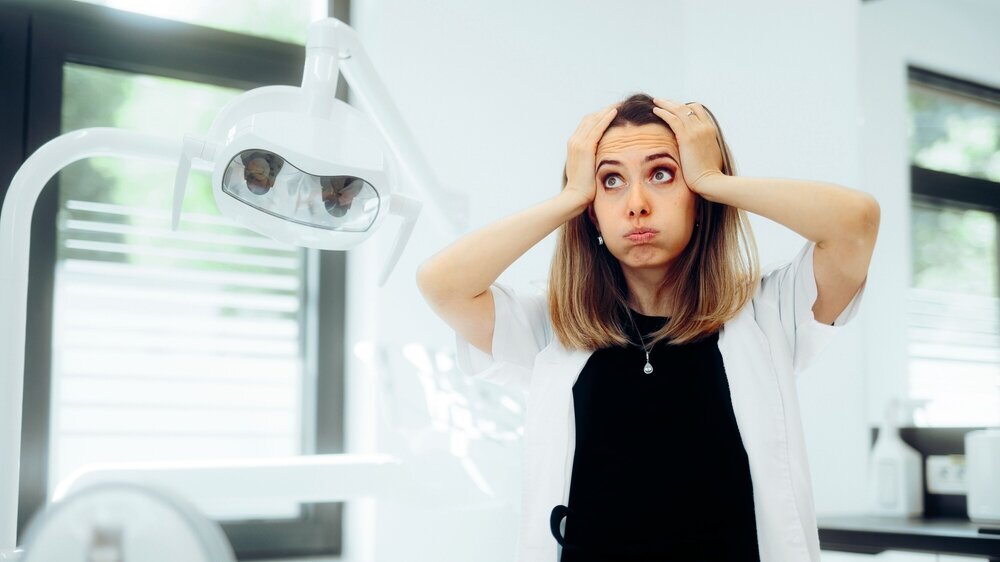 Gestresste Zahnärztin, die besorgt in ihrem Behandlungszimmer steht.