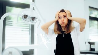 Gestresste Zahnärztin, die besorgt in ihrem Behandlungszimmer steht.