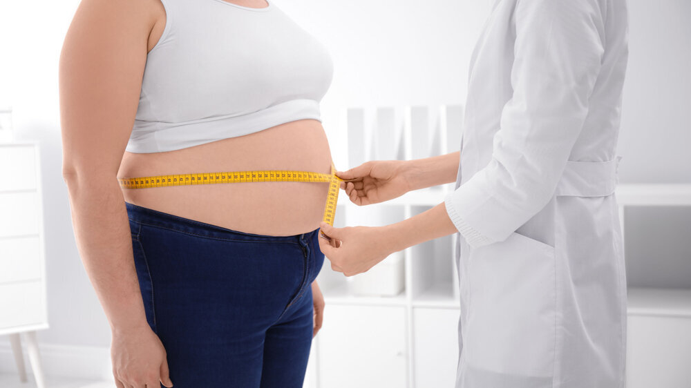 Doctor measuring waist of overweight woman in clinic, closeup