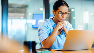 Geschäftsfrau, die in einer professionellen Büroumgebung konzentriert auf ihren Laptop schaut.