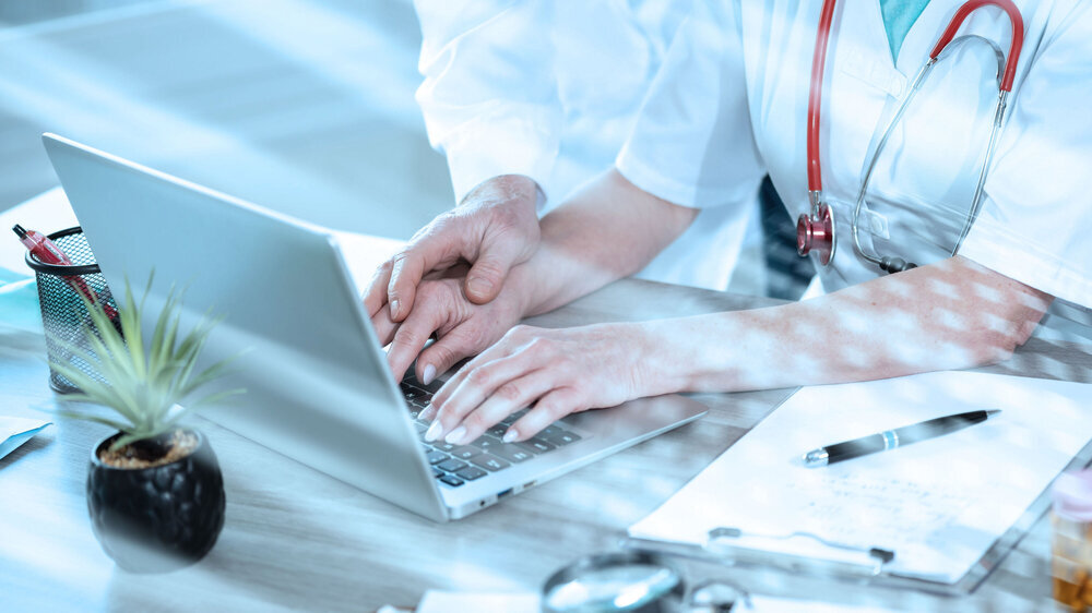 Themenfoto sexueller Übergriff im Gesundheitswesen - Mann legt seine Hand auf die einer am Laptop arbeitenden Frau Themenfoto sexueller Übergriff im Gesundheitswesen - Mann legt seine Hand auf die einer am Laptop arbeitenden Frau
