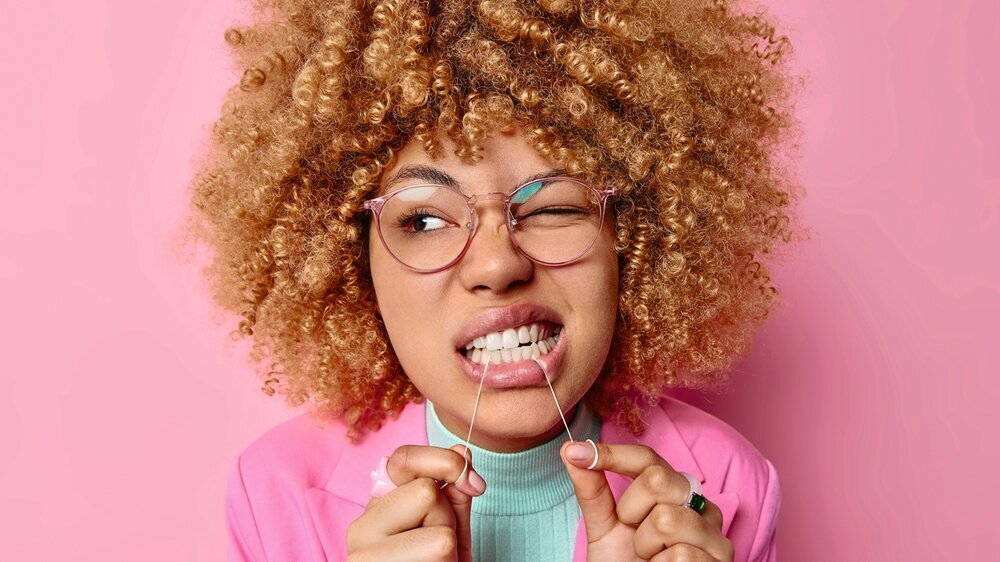 Junge Frau mit Brille und Afrolook nutzt Zahnseide Junge Frau mit Brille und Afrolook nutzt Zahnseide