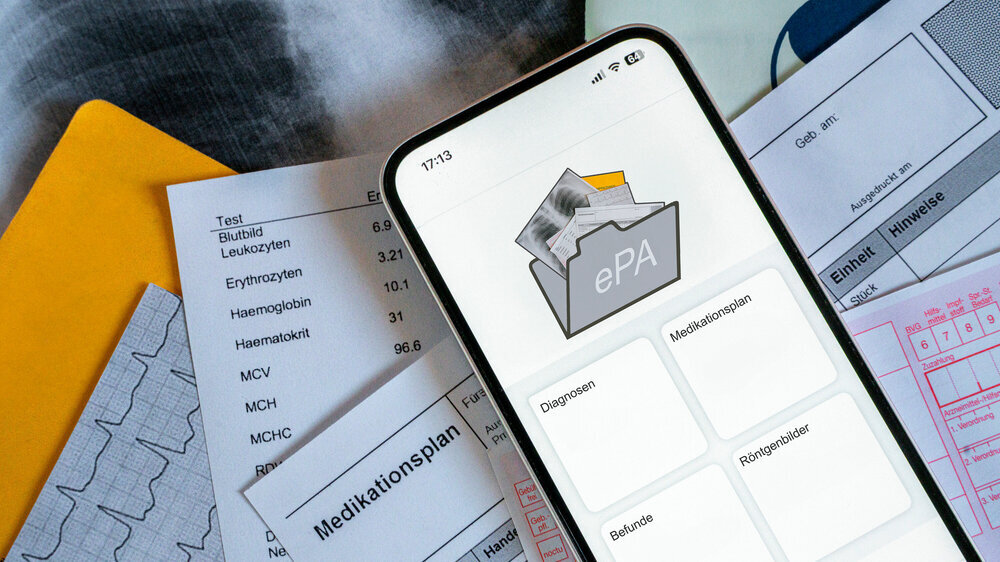 Ein Smartphone auf dem gerade eine elektronische Patientenakte angezeigt wird, liegt auf medizinischen Dokumenten, horizontal Ein Smartphone auf dem gerade eine elektronische Patientenakte angezeigt wird, liegt auf medizinischen Dokumenten, horizontal