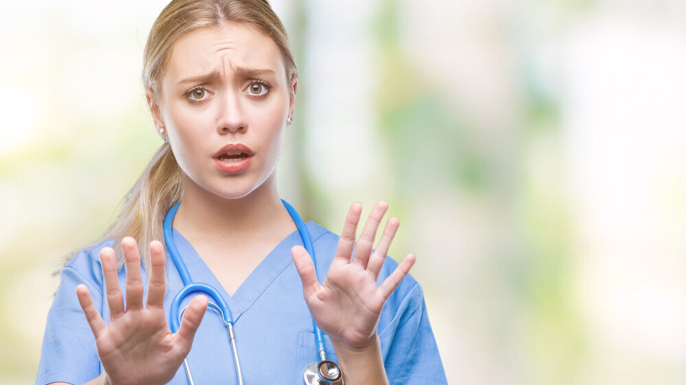Young blonde surgeon doctor woman over isolated background afraid and terrified with fear expression stop gesture with hands, shouting in shock. Panic concept. Krankenschwester MFA Krankenhaus Gewalt Angriff