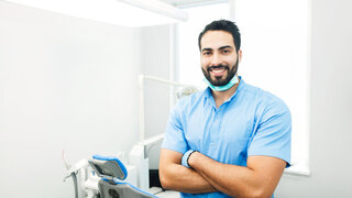 Portrait of hadsome dentist doctor wears blue uniform, indoor shot in modern dentist office