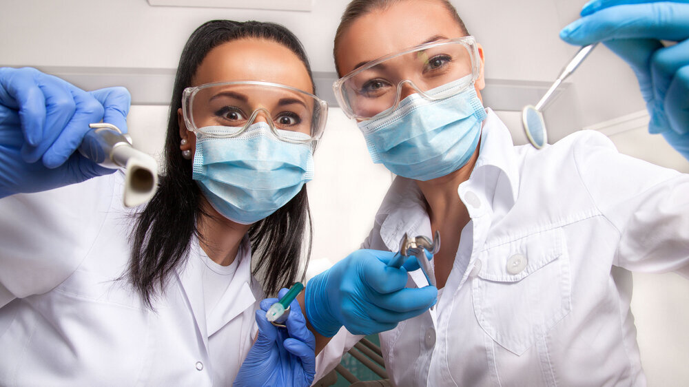 Female doctor dentist and assistant in masks looking at camera ZFA