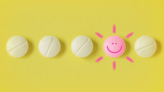 Pills in a row and pill with a happy face on yellow background - Concept of medicine, drug therapy and placebo effect